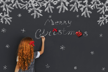 Little girl draws on chalkboard greeting card for your family. Marry Christmas holiday concept.の写真素材