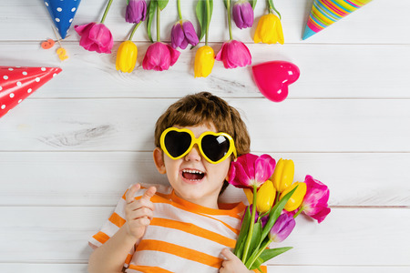 Laughing baby lying on the wooden floor with glasses for heart shape on carnival party. Healthy smiling, Mothers day, happy childhood concept.の写真素材