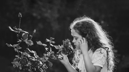 Little girl breathe scent of rose flowers. Black and white portrait in retro style.の写真素材
