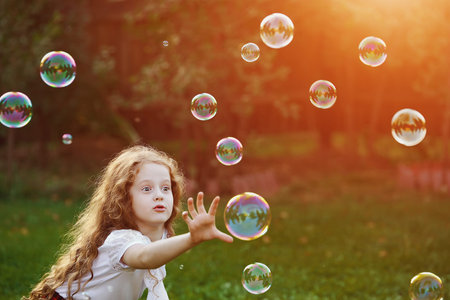 Crazy little girl catching soap bubbles in the summer park.