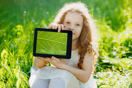 Child holds a tablet PC with a green leaf and studying biology in the park.の写真素材