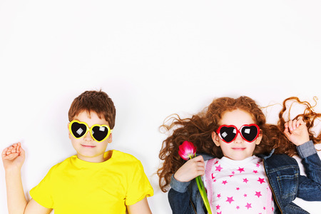 Funny children in sunglasses a heart shape, hold tulips and lies on the light floor. High top view background. Mother, Father or Valentines day concept.の写真素材