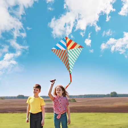 Children enjoy playing with a flying kite in meadow on sunny day.の写真素材