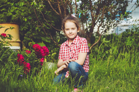 Curly baby girl near branch of peony in summer garden.の写真素材