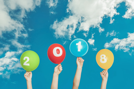 Child hand holding rainbow balloons with 2018 on blue sky and white clouds background.の写真素材