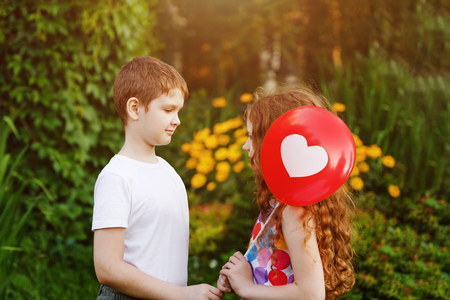 Cute little boy with gift red balloons with heart his friend girl in summer park. Valentines day background.の写真素材
