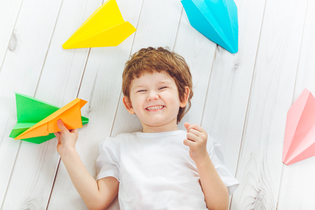 Smiling cute child with white t-shirt hold orange airplane and laying wooden floor. Vacation, education concept.の写真素材