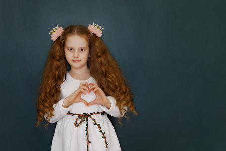 Little girl in white dress show heart gesture standing near green chalkboard. Healthy lifestyle or valentine's day concept.の写真素材