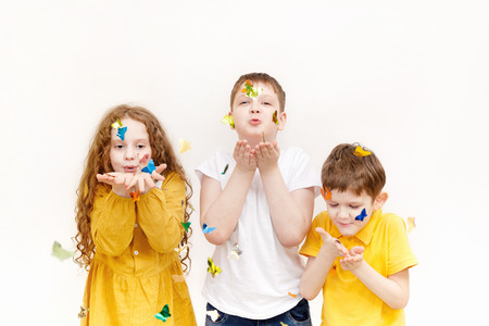 Cute little girl and boy blowing confetti on light background. Holiday concept.の写真素材