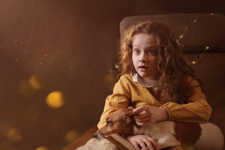 Surprised curly haired girl with a book and dog on her knees. Mystery, magic learning concept.の写真素材
