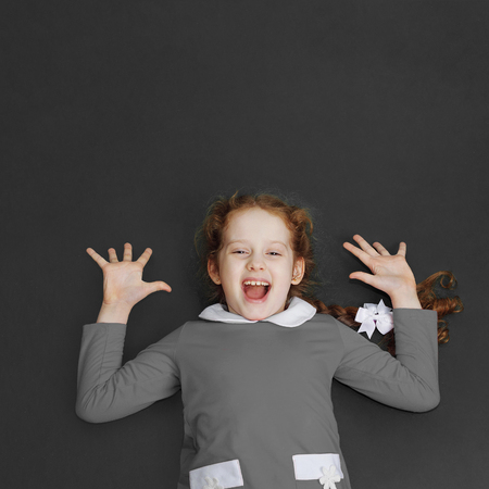 Laughing little girl standing near the blackboard. Back to school and easy learning concept.の写真素材
