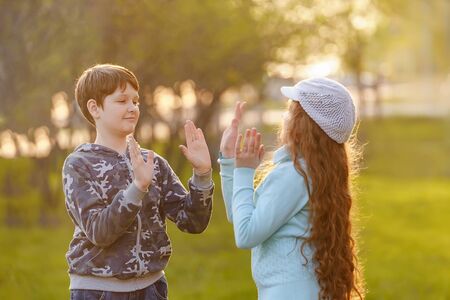 Happy child friend enjoying clapping hands, or playing patty cake, or giving high five having fun together in spring park.の写真素材