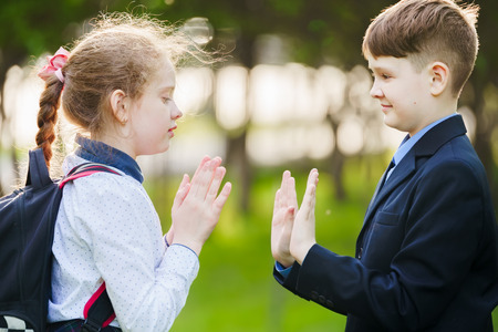 School child friend enjoying clapping hands, or playing patty cake, or giving high five having fun together in spring park.の写真素材