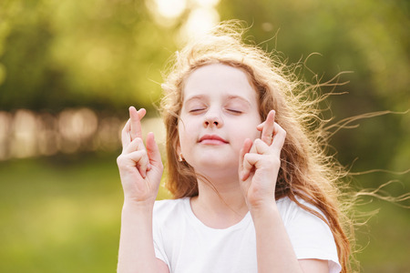 Little redhead girl  raises fingers crossed and makes desirable wish outdoors.の写真素材