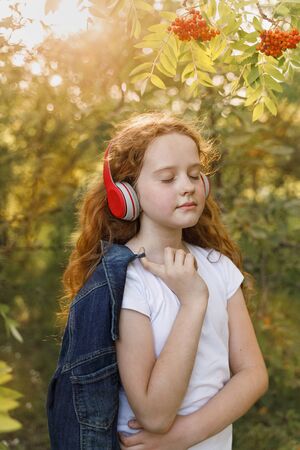 Little girl listening to music on headphones in a summer park.の写真素材