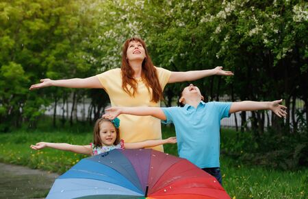 Happy family standing in the rain with a multi-colored umbrella catches raindropsの写真素材