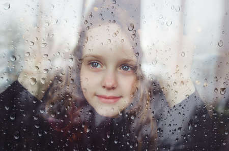 Sad little girl look out the window during the coronavirus outbreak. Quarantine, Covid-19 isolation. Self-isolate concept.の写真素材
