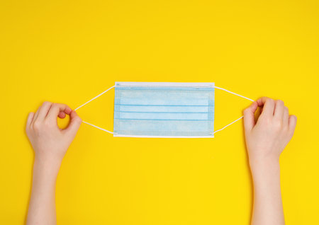Child hands holding medical mask. High top view on yellow background. Protection, healthy,  concept.の写真素材