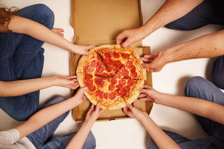 Family eating peperoni pizza. Kids and fathers holding a slice of pizza.の写真素材