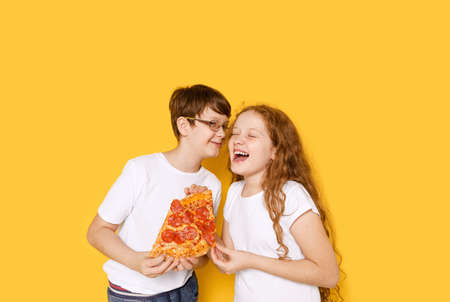 Funny boy and girl with pepperoni pizza on yellow background. Happy healthy smile concept.の写真素材