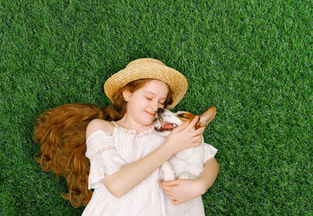 Cute girl and dog hugging, kissing and lying on the green grass in the spring park. Spring, Easter, friends concept.の写真素材
