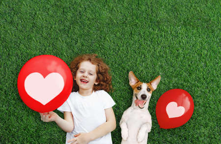 Laughing girl and puppy holding red balloon with heart. Mother's, Dad's, Valentine's Day concept. Happy spring day. Happiness concept.の写真素材
