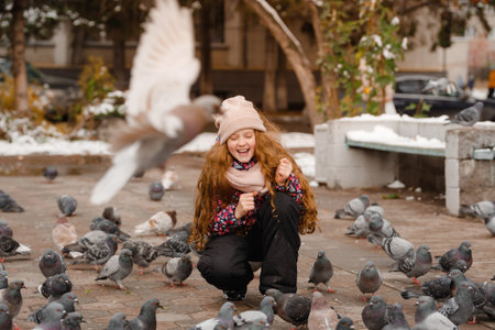 Cute girl is feeding pigeons with nice winter day outdoors.の写真素材