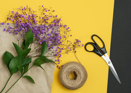 Bouquet of pink flowers, rope, craft paper, scissors on the yellow background, top view.