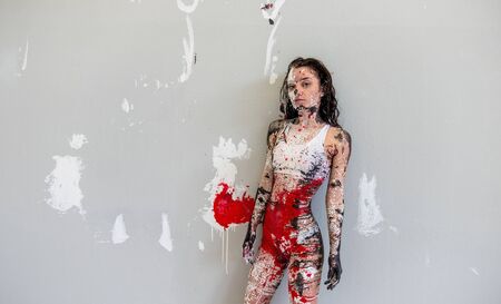 Young sexy woman in underwear, sportswear, artistically abstract painted with black red white, paint, rolls off in front of white wall in studio and leaves colorful color prints, copy space.の写真素材