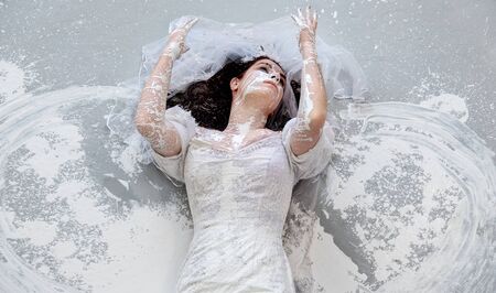 upper body, of a beautiful young artistically abstract painted woman, bride, like snow-white in wedding dress with white paint, creative, abstract body art, on the floor in the studio, copy space.の写真素材