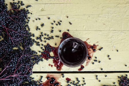 Fresh ripe violet black elderberries, squeezed and pressed and elderberry juice, on rustic grey yellow table background with free space for your text, copy spaceの写真素材
