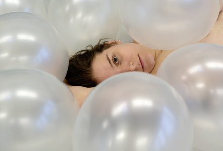 Portrait art view from above to beautiful young woman face with brunette hair between white iridescent balloons, beauty fashion concept, copy spaceの写真素材