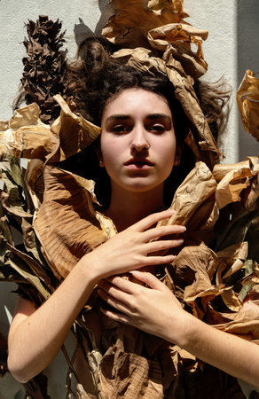 Portrait of young sexy brunette woman covered by leaves of dry, withered decorative banana tree,...