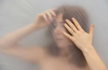 Blurred, out of focus portrait of beautiful sexy seductive lockdown sensual redhead headache woman behind plastic film foil in isolation, copy spaceの写真素材