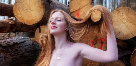 sensual, seductive portrait of young beautiful sexy redhead woman plays smiling with her beautiful gorgeous red hair in front of a wood pile in the forest, copy spaceの写真素材