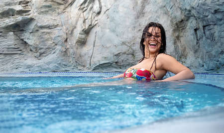 Beautiful brunette, young, sexy woman with dark hair relaxes contend happy in colorful flower bikini in holidays summer sun in the blue spa wellness whirlpool, copy spaceの写真素材