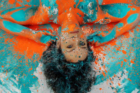 unusual remarkable impressive portrait of adult brunette curly woman, dots of green turquoise and orange color paint, decorative creative expressive abstract body painting art, make up, copy spaceの写真素材