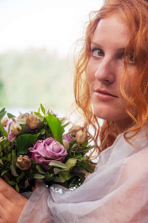 close-up of a seductive young sexy redhead beautiful sensual woman portrait, ginger with long curly hair, outdoor with a bouquet of wilted flowers, copy spaceの写真素材