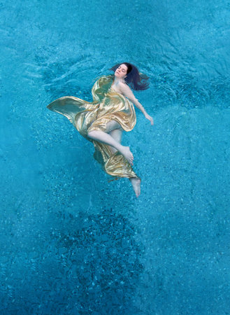 Top view of a beautiful young sexy mermaid woman in golden dress, evening dress cape, floating...
