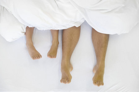 Close up of four feet, male and female, in bed lying side by side, copy space
