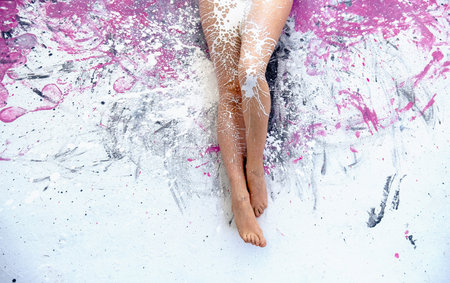beautiful woman legs with white paint splashed on the pink and gray painted studio floor