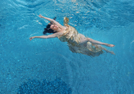 beautiful dark-haired woman with curls relaxed in golden towel floats happily floating in the...