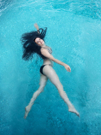 beautiful mature woman in the best age with dark curly hair in a bikini is running floating...
