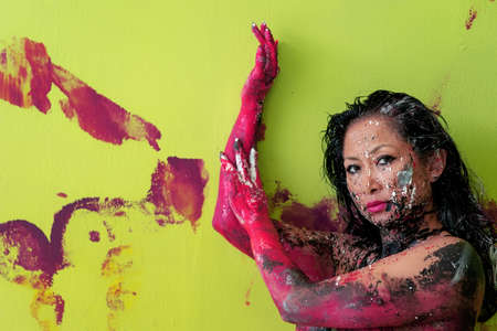 Portrait, arms and hands of artistically painted with color abstractly painted asian woman in pink and green, creative, abstract body art, body painting, action painting, art painting and pushing the paint on the wall.の写真素材