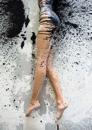 beautiful legs and feet of a sexy young artistically abstract painted woman in underwear, sportswear, with black and white paint, lying on the colorful painted floor in the studio, copy space.の写真素材
