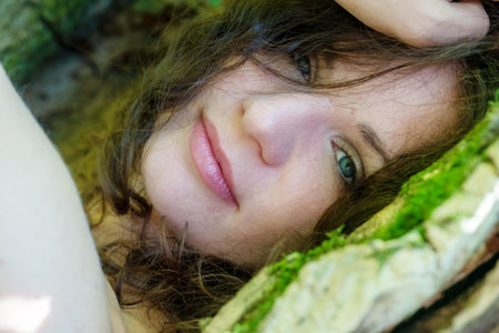 Portrait of a beautiful dark-haired young sexy woman lying happily contentedly in bed of moss in the...