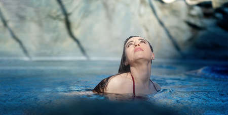 Portrait of beautiful mature woman with dark hair relaxes contend happy in holidays summer sun in the blue spa wellness whirlpool, raised eyes, looking up to the sunny sky, copy spaceの写真素材
