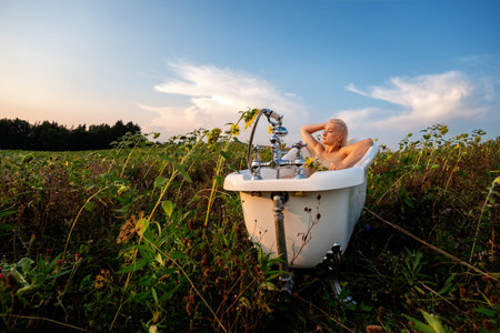 rural landscape with young beautiful sexy blonde woman taking a bath in nature in the sunset in a...