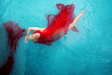 Beautiful sexy blonde young woman swimming with red cloths wrapped in clear turquoise blue pool water, copy spaceの写真素材