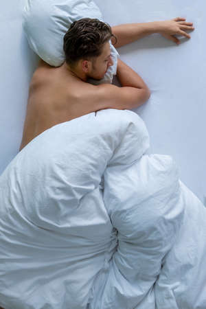 Bed time. Top view of the portrait and back of a shirtless muscular young man in bed in the morning, copy spaceの写真素材